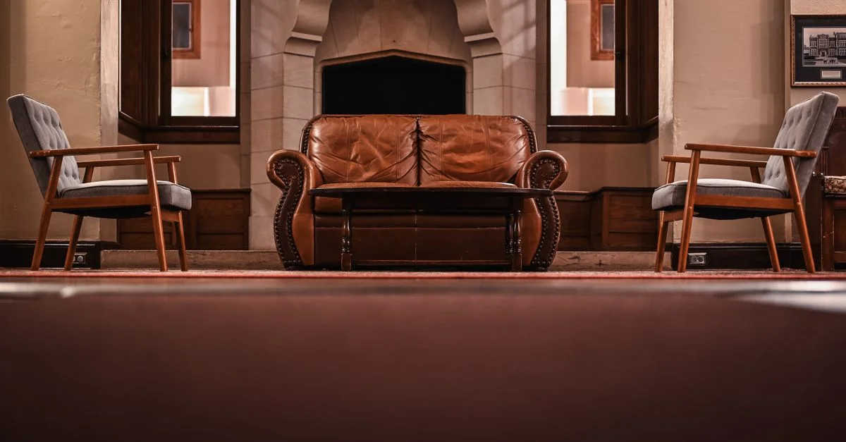 Un salon au style vintage avec un canapé en cuir, des fauteuils et une cheminée classique.