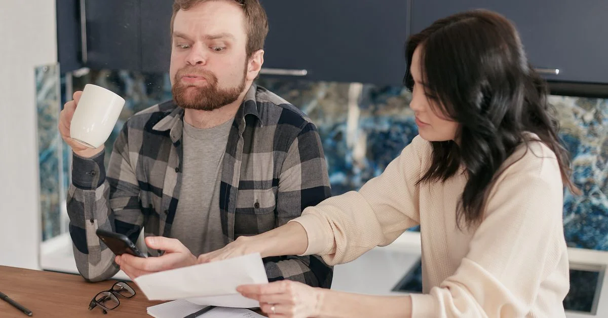 Un couple a l'air inquiet alors qu'il consulte des factures à leur table de cuisine, reflétant des préoccupations financières.