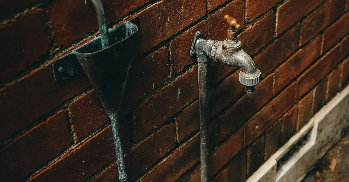 Gros plan d'un robinet extérieur rouillé attaché à un mur en brique usé.