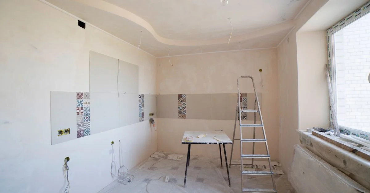 Cuisine spacieuse en cours de rénovation, avec échelle et outils, dévoilant un tout nouveau design.