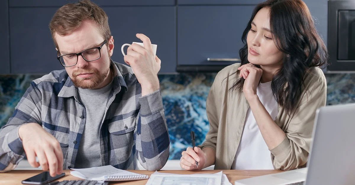 Un jeune couple concentré sur la révision de documents et la gestion de leur budget à la maison, mettant en avant les défis financiers modernes.