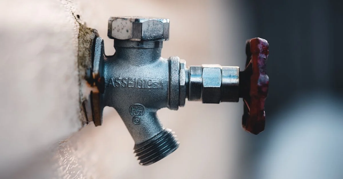 Gros plan détaillé d'un robinet en métal monté sur un mur extérieur avec des textures visibles.