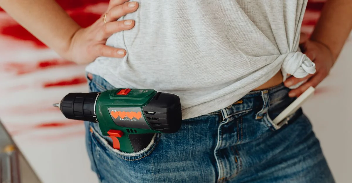 Gros plan d'une personne avec une perceuse à batterie rangée dans un jean en denim, prête à travailler.