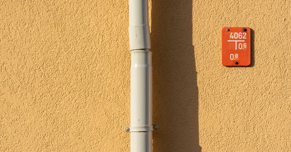 Gros plan sur un mur texturé jaune avec un tuyau en métal et un panneau de numéro rouge.