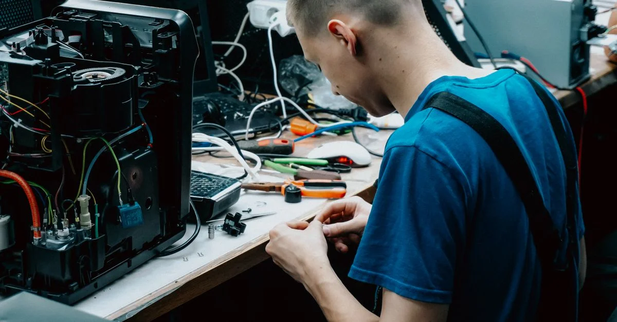 Technicien qualifié assis à un banc de travail réparant des appareils électroniques dans un cadre d'atelier.