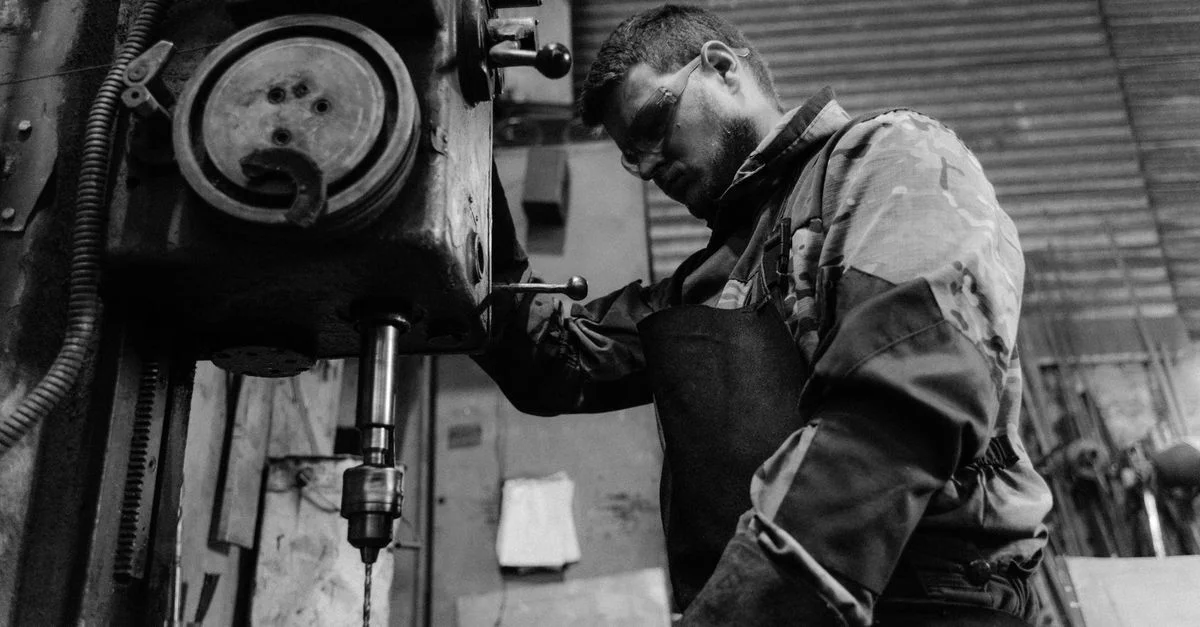 Photo en noir et blanc d'un travailleur concentré sur l'utilisation d'une perceuse, mettant en avant l'artisanat.