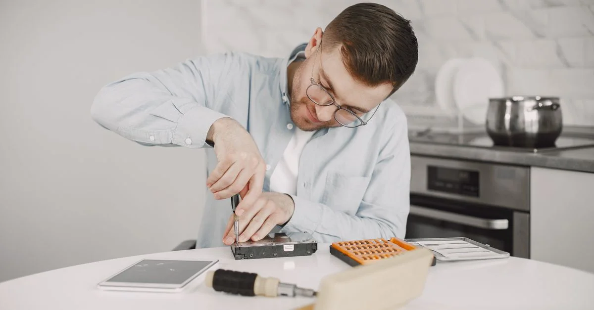 Homme portant des lunettes utilisant un tournevis pour réparer un appareil sur une table de cuisine.