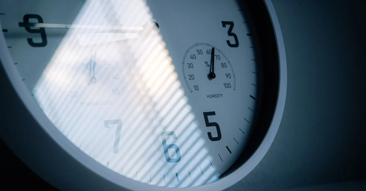 Un gros plan d'une horloge murale affichant l'heure et l'humidité, réfléchissant la lumière et les ombres.