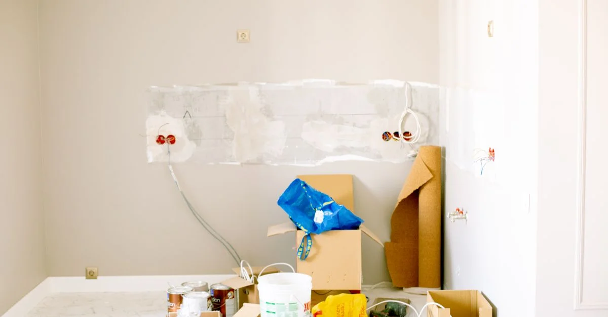 Une chambre en cours de rénovation avec des outils, des fournitures, du câblage et des seaux de peinture éparpillés autour.
