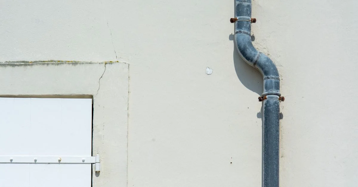 Gros plan d'un tuyau de drainage en métal gris attaché à un mur extérieur simple.