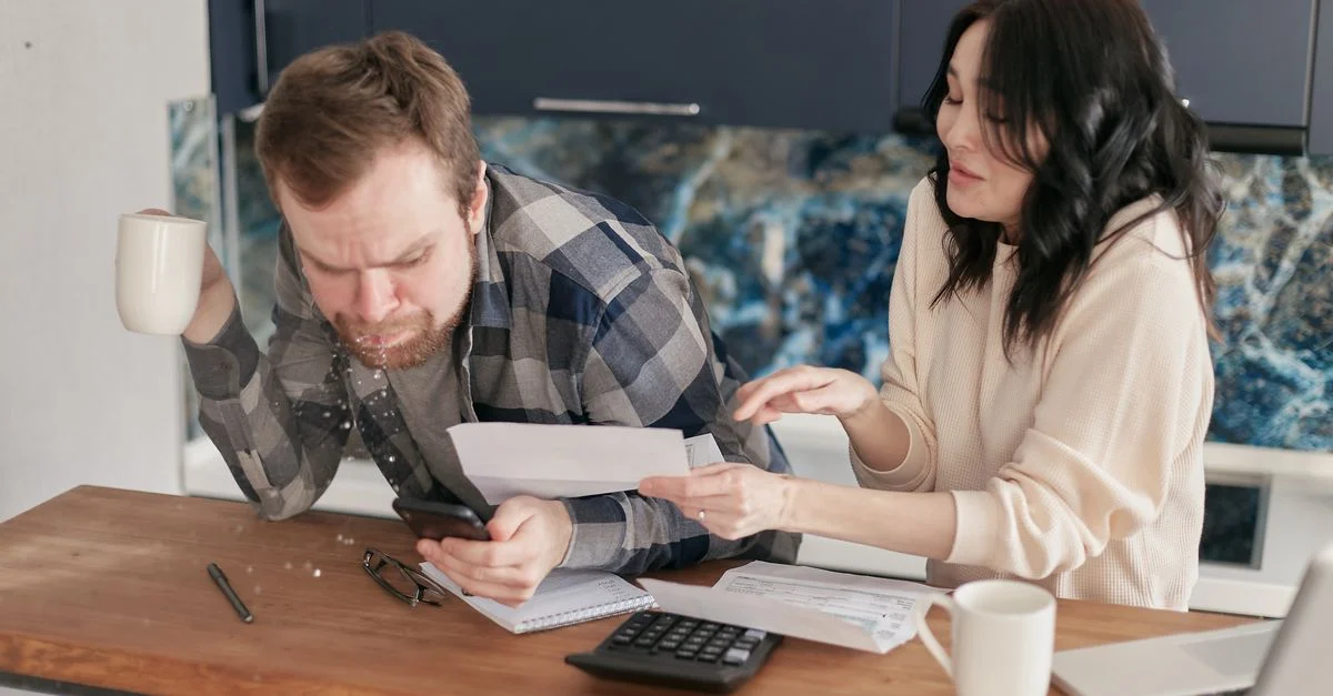 Un couple assis à un bureau, examinant des factures et des dépenses avec une calculatrice et un ordinateur portable, l'air inquiet.